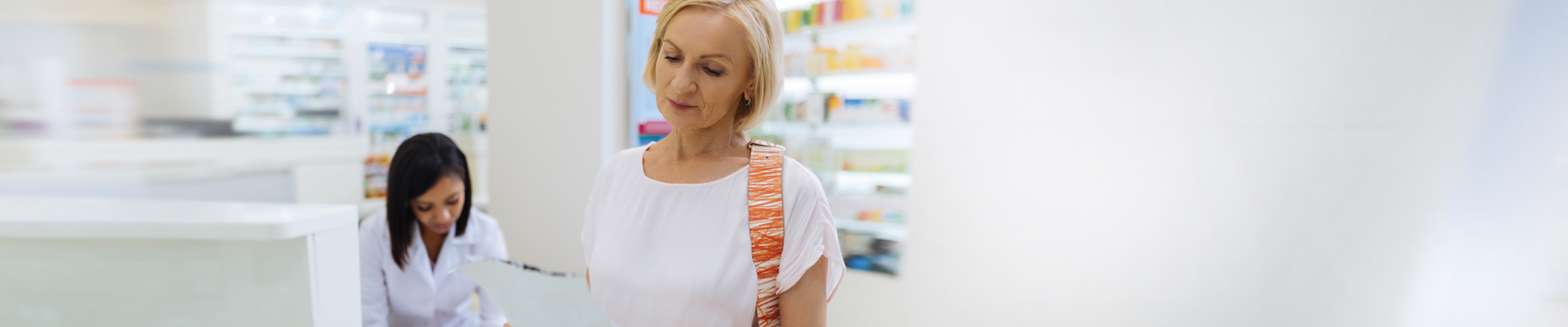 Woman looking at prescription at doctors’ office with health care provider in background
