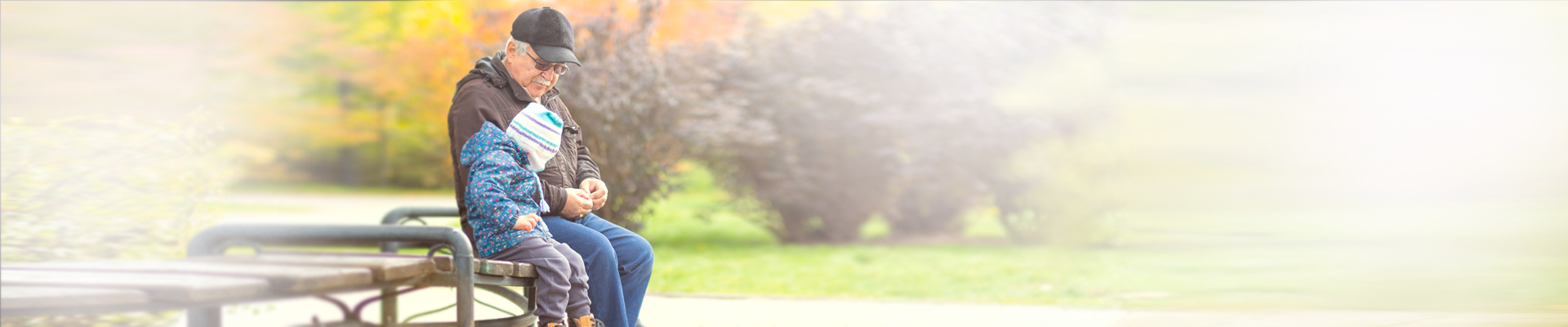 Young child sitting on park bench with older man