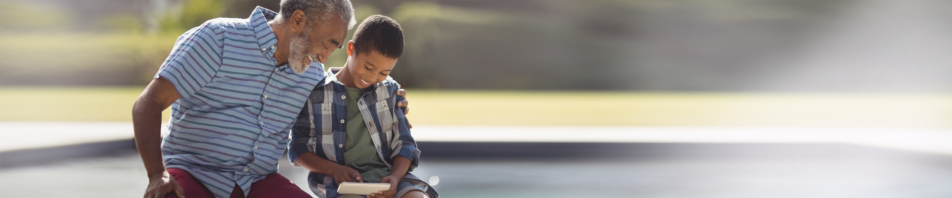 Older man with arm around younger boy sitting outside looking at phone 